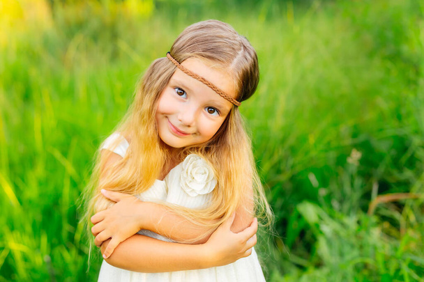 Uśmiechnięta dziewczyna na zielonej łące, małe dziecko przytula się, ubrana w białą sukienkę i bandaż na czole. - Zdjęcie, obraz