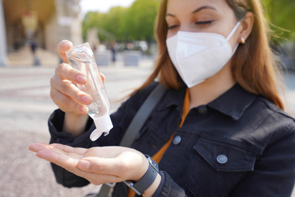 Detailní záběr krásné mladé ženy na sobě KN95 FFP2 ochranné masky pomocí alkoholu gel dezinfikující její ruce na ulici města. Zaměření na ruce. - Fotografie, Obrázek