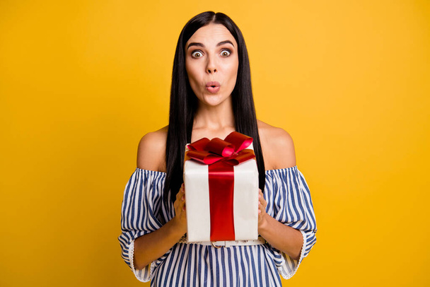 Photo of cute excited young lady wear striped dress getting gift box lips pouted isolated yellow color background - 写真・画像