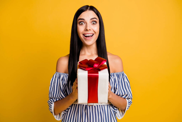 Photo of impressed funny young woman dressed off-shoulders dress holding present box big bow isolated yellow color background - Φωτογραφία, εικόνα