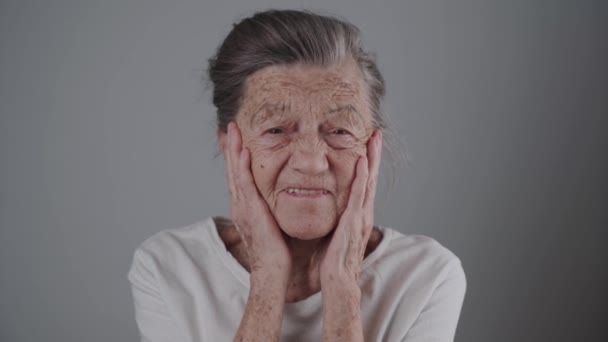 Donna anziana sorridente con dentiera in studio su sfondo grigio. Positività e longevità. Pensionato si sente soddisfatto. Non si è mai vecchi per essere felici. Allegro anziana donna ridere - Filmati, video