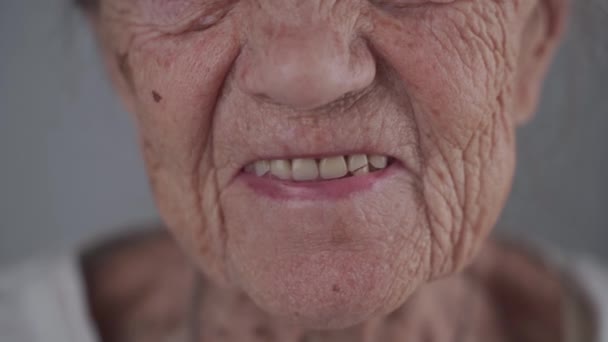Крупным планом довольна белая старшая женщина, смотрящая в камеру улыбаясь и смеясь над серым фоном. Портрет бабушки 90 лет счастливой в студии. Зубной протез для пожилых людей - Кадры, видео