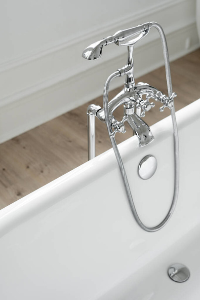 Srebrny prysznic i kran nad białą pustą wanną. Klasyczna kąpiel z chromowanym kranem w nowoczesnym wnętrzu łazienki w stylu skandynawskim - Zdjęcie, obraz