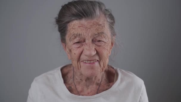 Señora mayor sonriente con dentadura postiza en el estudio sobre fondo gris. Positividad y longevidad. Pensionista sintiéndose satisfecho. Nunca eres demasiado viejo para ser feliz. alegre anciana riendo - Metraje, vídeo