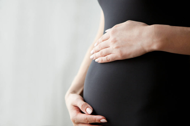 Schwangerschaftsbauch - Schwangere berührt ihren Bauch mit den Händen, Nahaufnahme - Foto, Bild