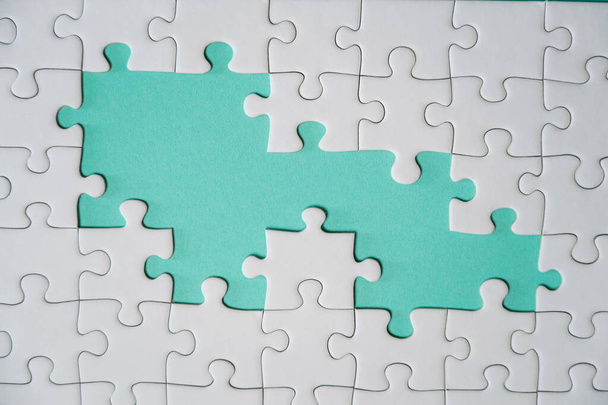 Missing jigsaw puzzle pieces. Business concept. Fragment of a folded white jigsaw puzzle and a pile of uncombed puzzle elements against the background of a colored surface. - Photo, Image