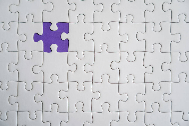 Ontbrekende puzzelstukjes. Bedrijfsconcept. Fragment van een gevouwen witte legpuzzel en een stapel ongekamde puzzelelementen tegen de achtergrond van een violet oppervlak. - Foto, afbeelding
