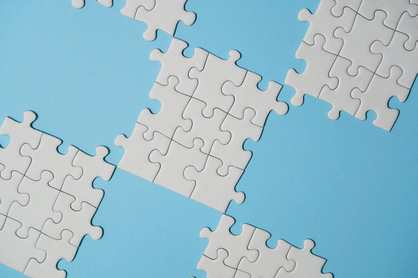 Missing jigsaw puzzle pieces. Business concept. Fragment of a folded white jigsaw puzzle and a pile of uncombed puzzle elements against the background of a blue surface. - Фото, изображение