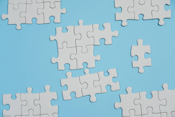 ジグソーパズルの欠片。ビジネスコンセプト。折り畳まれた白いジグソーパズルの断片と青い表面の背景を背景にした妥協のないパズル要素の山. - 写真・画像