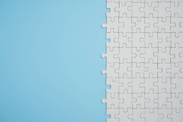 Missing jigsaw puzzle pieces. Business concept. Fragment of a folded white jigsaw puzzle and a pile of uncombed puzzle elements against the background of a blue surface. - Photo, image