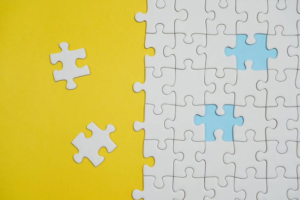 Missing jigsaw puzzle pieces. Business concept. Fragment of a folded white jigsaw puzzle and a pile of uncombed puzzle elements against the background of a yellow surface. - Photo, Image