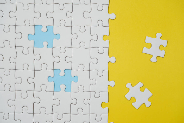 Missing jigsaw puzzle pieces. Business concept. Fragment of a folded white jigsaw puzzle and a pile of uncombed puzzle elements against the background of a yellow surface. - Φωτογραφία, εικόνα