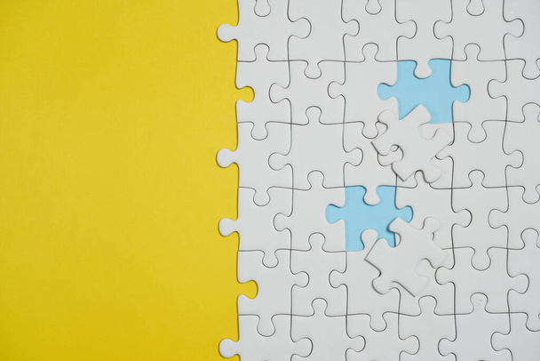 Missing jigsaw puzzle pieces. Business concept. Fragment of a folded white jigsaw puzzle and a pile of uncombed puzzle elements against the background of a yellow surface. - Photo, image