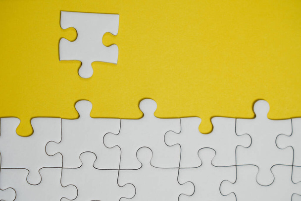 Missing jigsaw puzzle pieces. Business concept. Fragment of a folded white jigsaw puzzle and a pile of uncombed puzzle elements against the background of a yellow surface. - Photo, Image