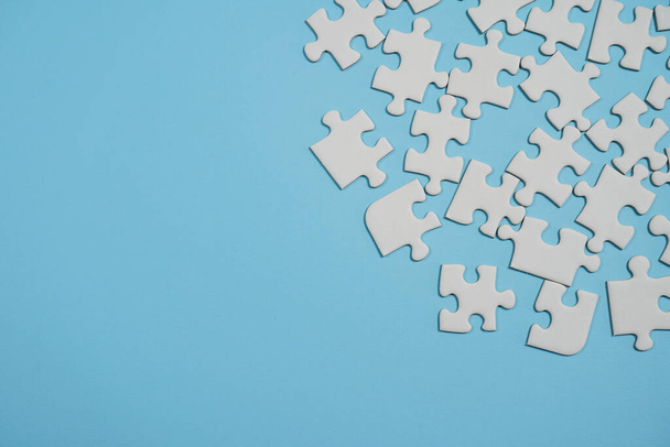 Missing jigsaw puzzle pieces. Business concept. Fragment of a folded white jigsaw puzzle and a pile of uncombed puzzle elements against the background of a blue surface. - Photo, Image