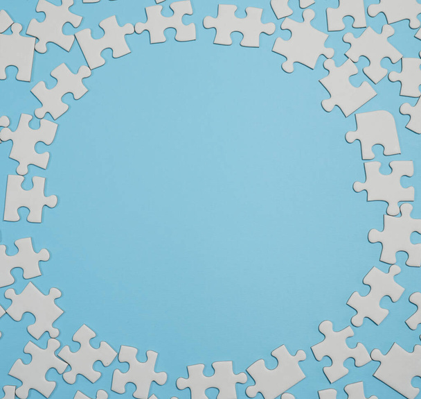 Missing jigsaw puzzle pieces. Business concept. Fragment of a folded white jigsaw puzzle and a pile of uncombed puzzle elements against the background of a blue surface. - Photo, image