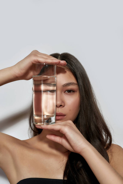 Young asian woman hiding face behind glass with water - Фото, изображение