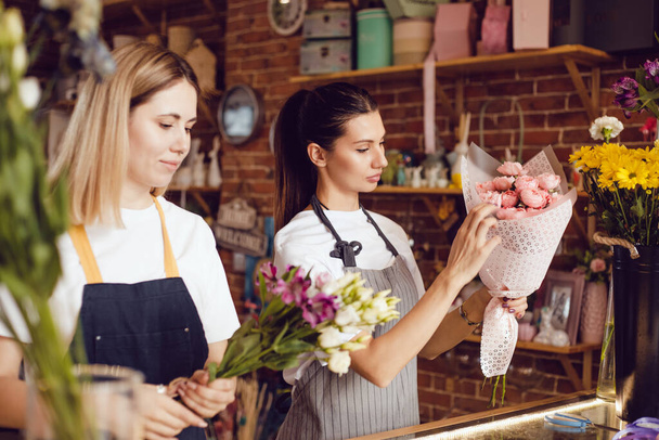 Woman florist together with assistant collect bouquets in flower shop. - Φωτογραφία, εικόνα
