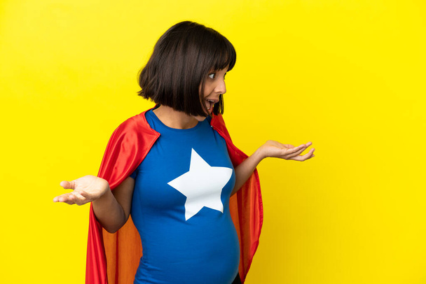 Super Hero pregnant woman isolated on yellow background with surprise expression while looking side - Photo, Image