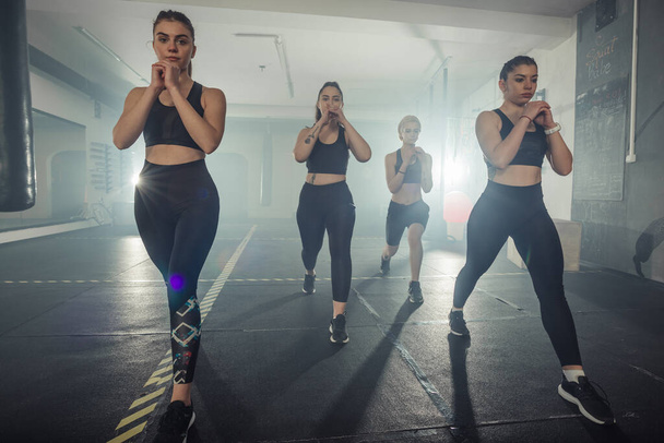 Group of sportswomen in sportswear doing lunge exercise at the gym with their left leg - Photo, Image