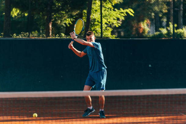 プロの設備の整った男性テニスプレーヤーが前手でテニスボールを強く打つ - 写真・画像