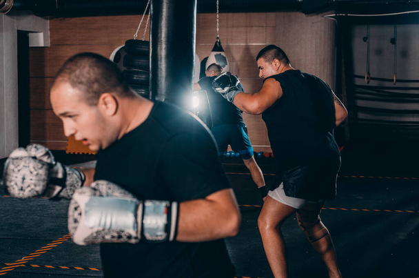Mannelijke bokser training met bokszak in donkere sporthal. Man bokser als oefening voor het grote gevecht. Boxer slaat bokszak - Foto, afbeelding