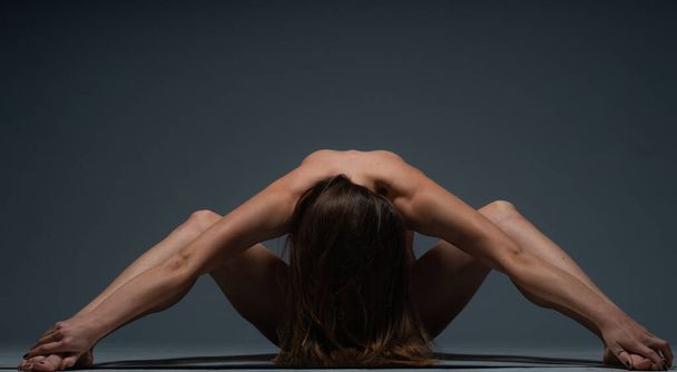 Do góry nogami akrobatyczne zdjęcie młodej nagiej kobiety leżącej na podłodze w ciemnym studio - Zdjęcie, obraz