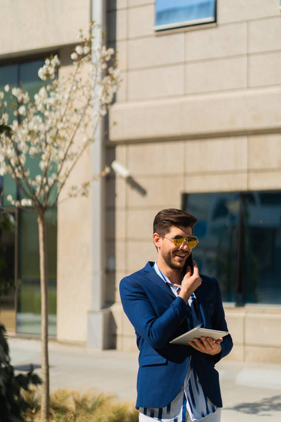 Stadtkaufmann lacht über die Angebote, die er am Telefon von seinen Geschäftspartnern bekommt, während er vor seiner Firma steht - Foto, Bild