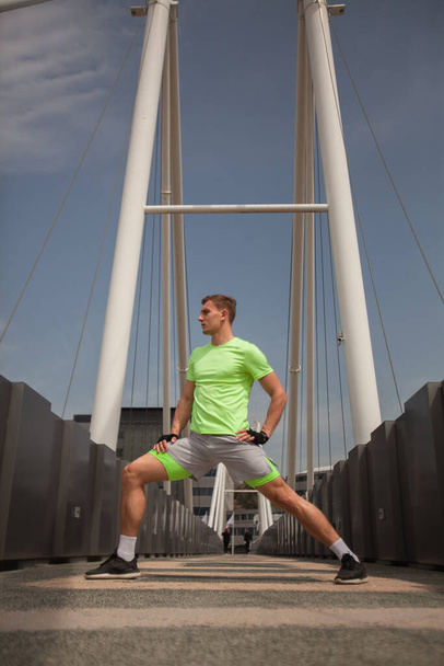 Ο δυνατός άντρας τεντώνει τα πόδια του στη μέση της γέφυρας. - Φωτογραφία, εικόνα