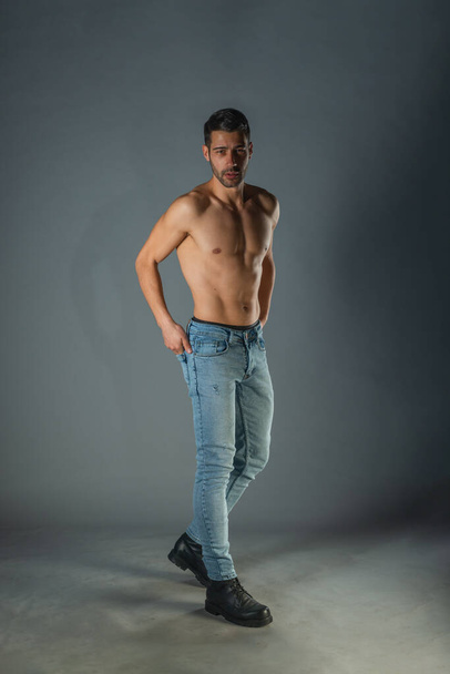Full body portrait of sports man with denim jeans posing with bare torso in a dark studio - 写真・画像