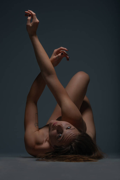Sexy full nude woman lying on her back and holding up her legs in a studio - Zdjęcie, obraz