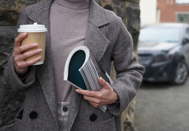 Fashion woman wearing coat , holding in hand  fashion magazine  and coffee cup. no face.  - Foto, immagini
