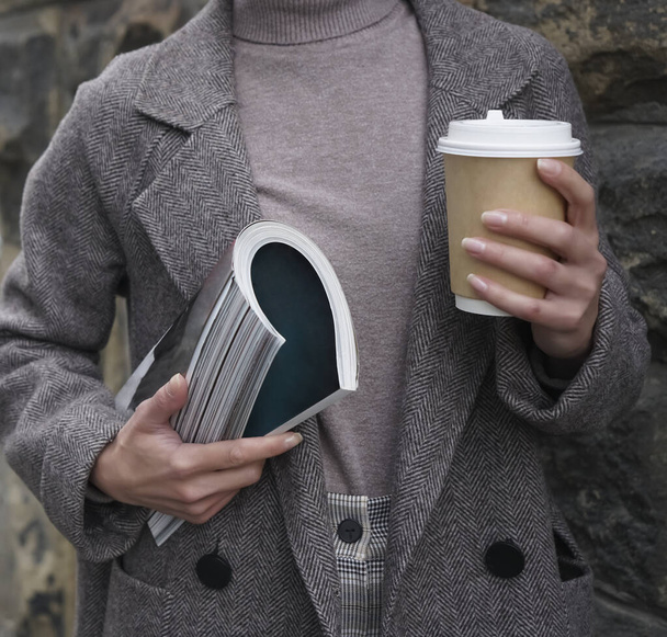 Fashion woman wearing coat , holding in hand  fashion magazine  and coffee cup. no face.  - Foto, Imagem