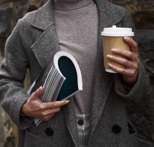 Fashion woman wearing coat , holding in hand  fashion magazine  and coffee cup. no face.  - Foto, immagini