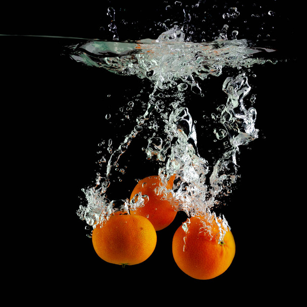 three tangerines fall into the water on a black background - Photo, image