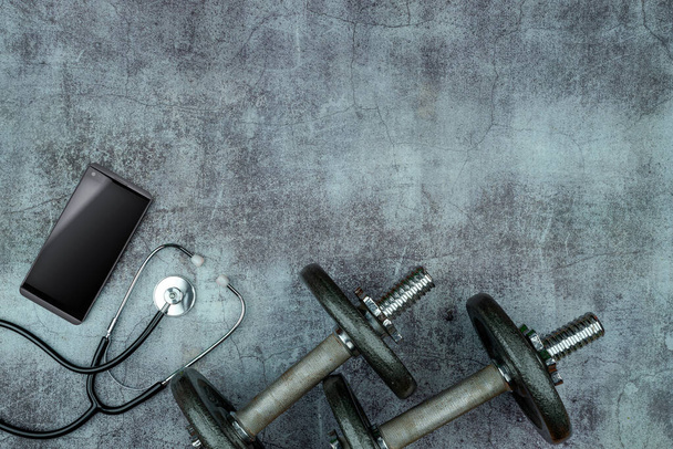 Gesundes Lifestyle-Powerlifting-Trainingskonzept mit gusseisernen olympischen Hantelscheiben, Stethoskop, Smartphone auf Zementboden. Leerer Kopierraum - Foto, Bild