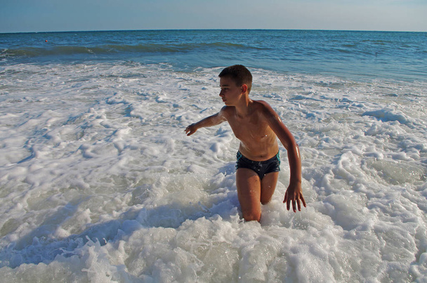 Jonge gebruinde jongen in een badpak verheugen zich in de zee stormgolven tijdens vakantie en reizen - Foto, afbeelding