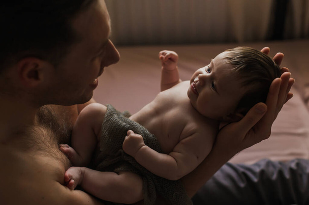Naked father holding a naked tiny baby in his arms. 3 months. Indoor. - 写真・画像