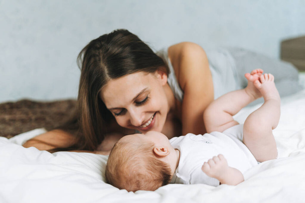 Young mother having fun with cute baby girl on the bed with white linen, natural tones, love emotion - Fotó, kép