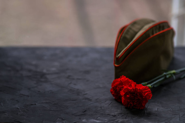 May 9, the Victory Day holiday. A holiday card with flowers and a military cap. Dark Background on May 9, copy space - Фото, изображение
