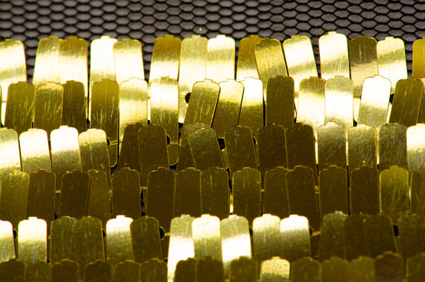 Sequins are golden. Ribbon for fabric decoration. Background texture, sunrise. Smooth slope of rows of round amber sequins on a fine fabric mesh. - Photo, Image