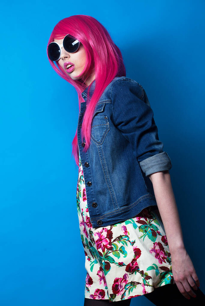 Young fashion female model with pink hair and big sunglasses over blue background - Fotoğraf, Görsel