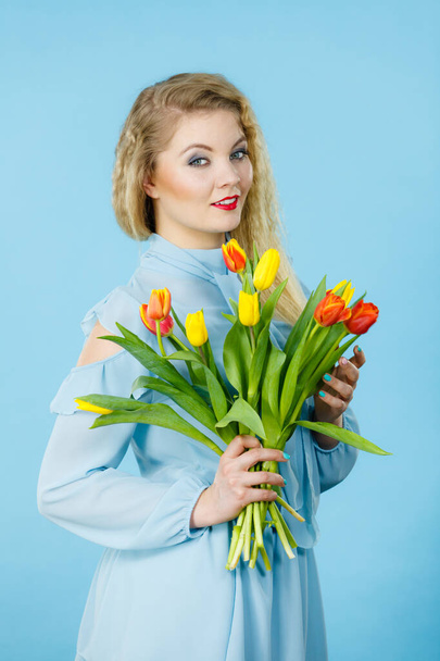 International women day, eight march. Beautiful portrait of pretty woman blonde hair with red yellow tulips, fashion make up, elegant dress. Mother day. On blue - Фото, изображение