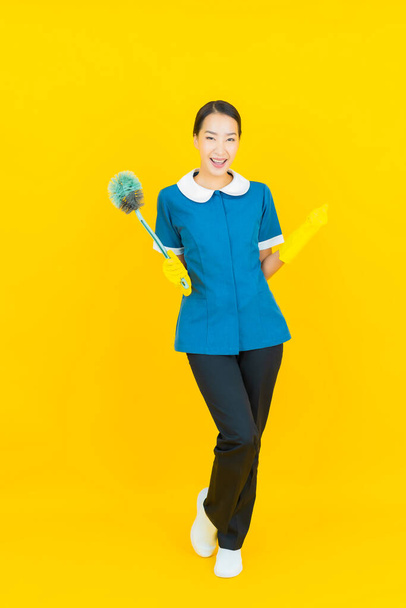 Retrato hermosa joven asiática mujer mucama y limpieza sonrisa con acción en color amarillo fondo - Foto, imagen