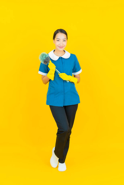 Πορτρέτο όμορφη νεαρή Ασιάτισσα υπηρέτρια και housekeping χαμόγελο με δράση σε κίτρινο χρώμα φόντο - Φωτογραφία, εικόνα