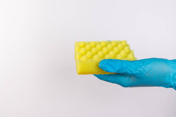 Naisten käsi sinisissä käsineissä kodin puhdistus- ja puhdistusaineita varten pitää keltaista sientä eristetyllä valkoisella taustalla - Valokuva, kuva