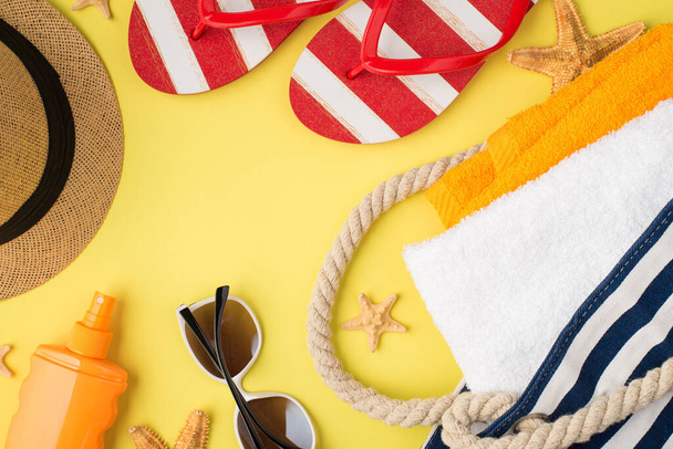 Вид зверху фотографія морської пляжної сумки з помаранчевими та білими рушниками сонцезахисні окуляри для пляшок та фліп-флоп на ізольованому жовтому фоні
 - Фото, зображення