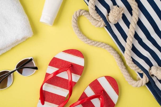 Top view photo of white towel cream bottle beach bag striped flip-flops and sunglasses on isolated pastel yellow background - Foto, Imagen