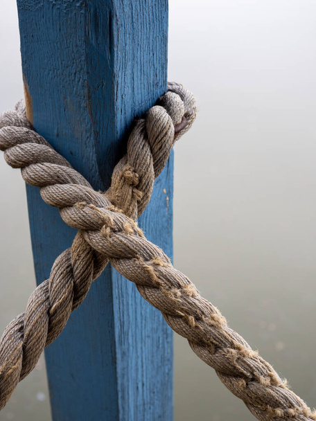 A vertical shot of a rope tied around a blue wooden column - Фото, изображение