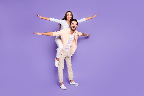Full length profile photo of two cheerful persons piggyback arms flying toothy smile isolated on violet color background - Фото, зображення